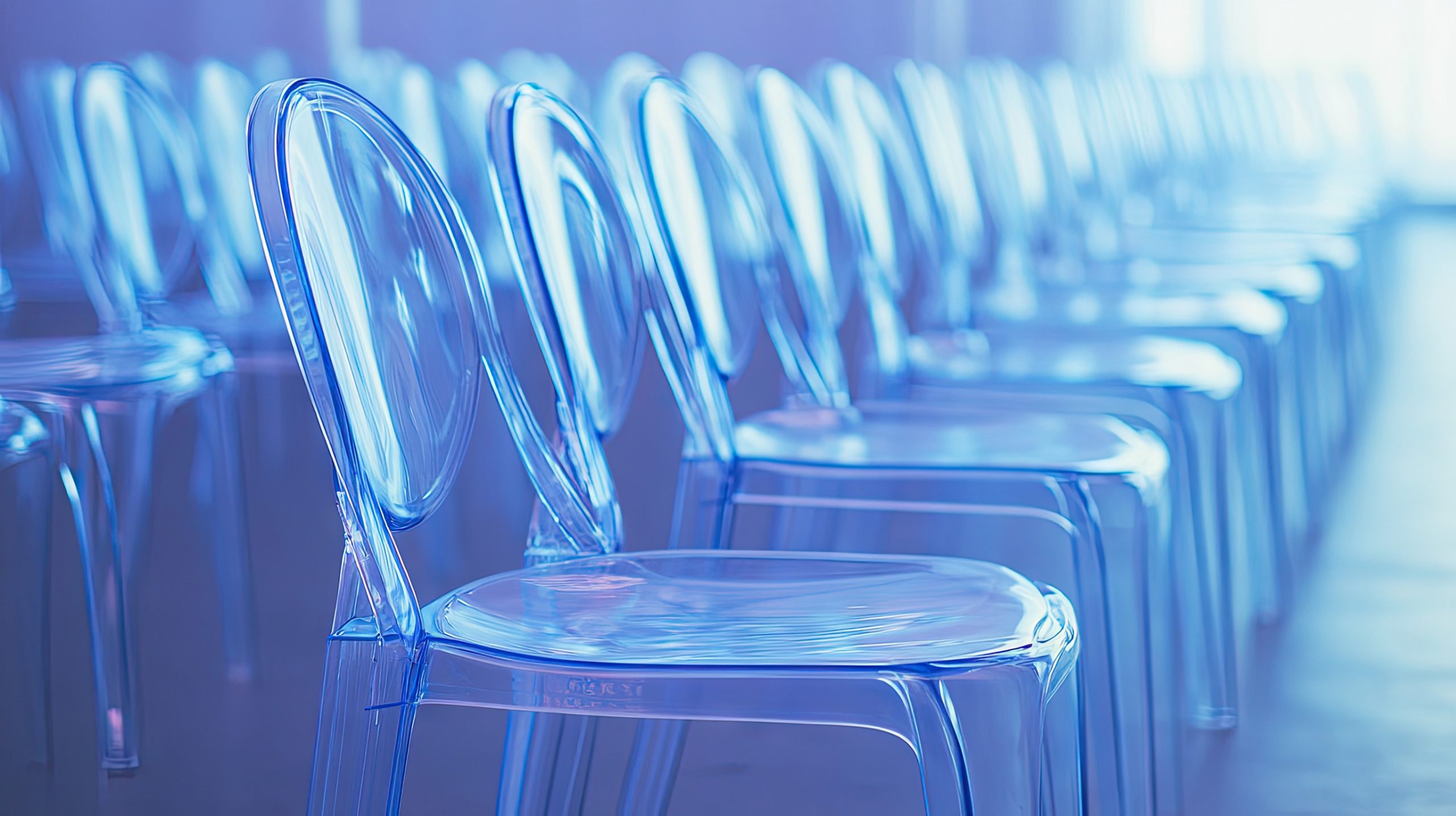Transparent ghost chairs arranged in a modern indoor space, creating a stylish and contemporary atmosphere with soft purple and blue lighting effects.